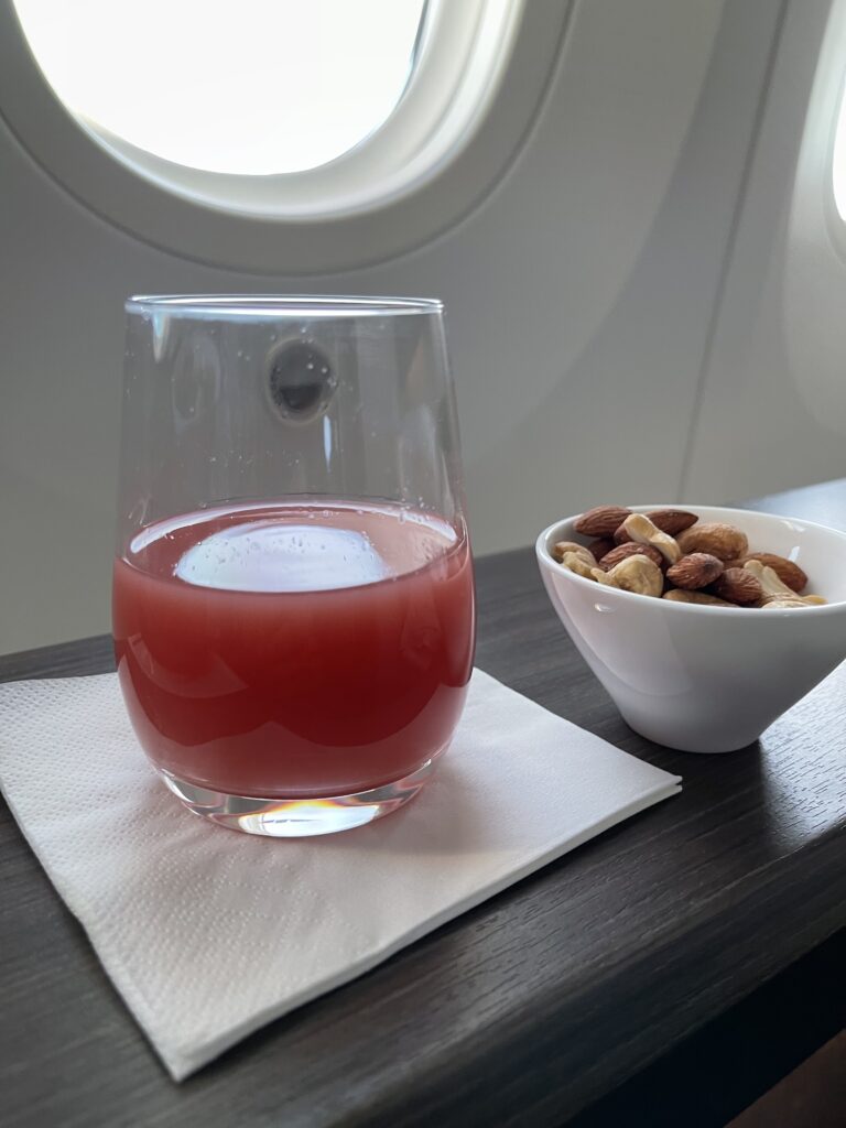 a glass of red liquid next to a bowl of nuts