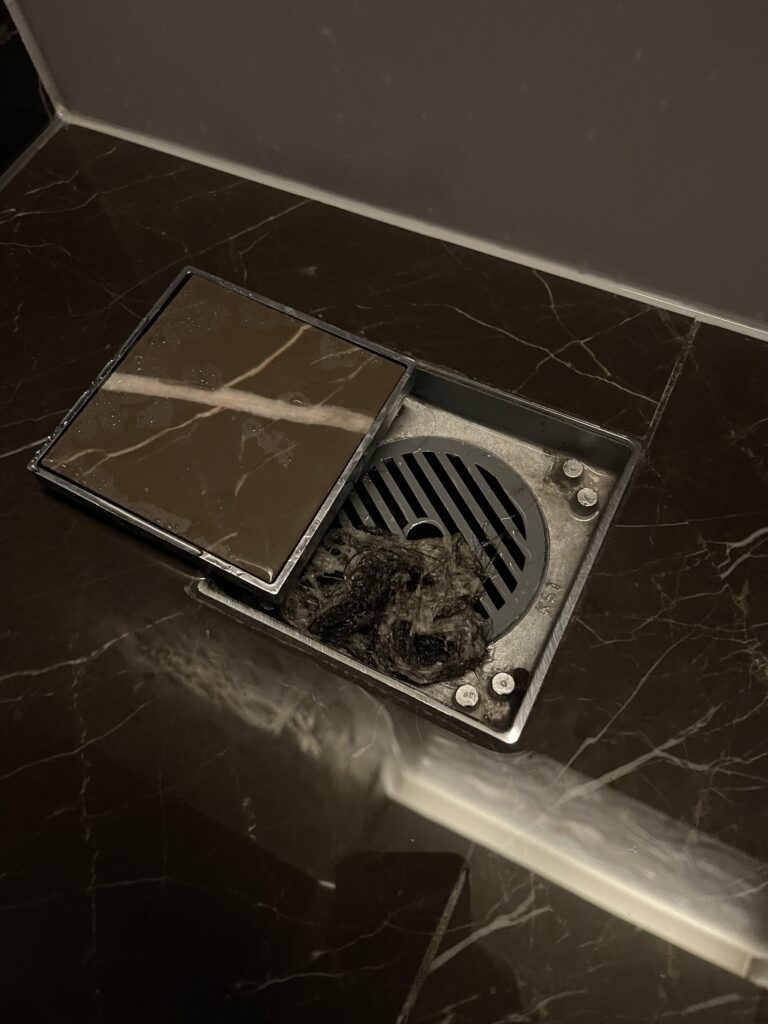 a square metal drain with a black cover on a marble counter