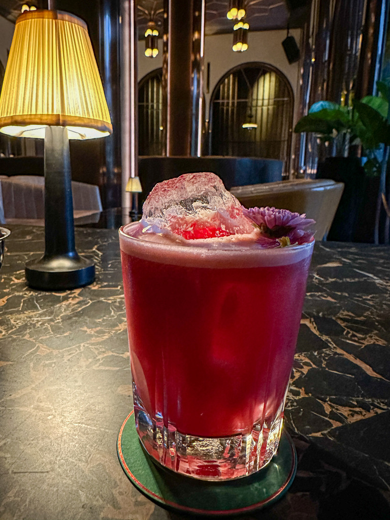 a glass of red drink with ice and flower on top