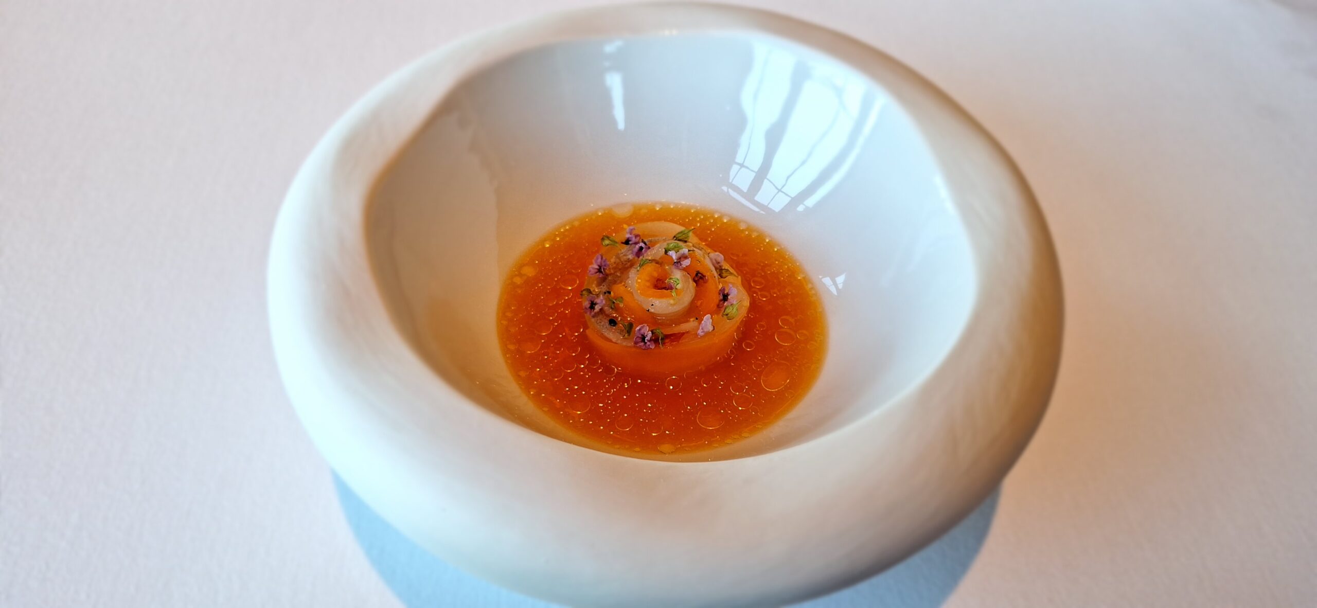 a white bowl with orange liquid and a spiral object in it