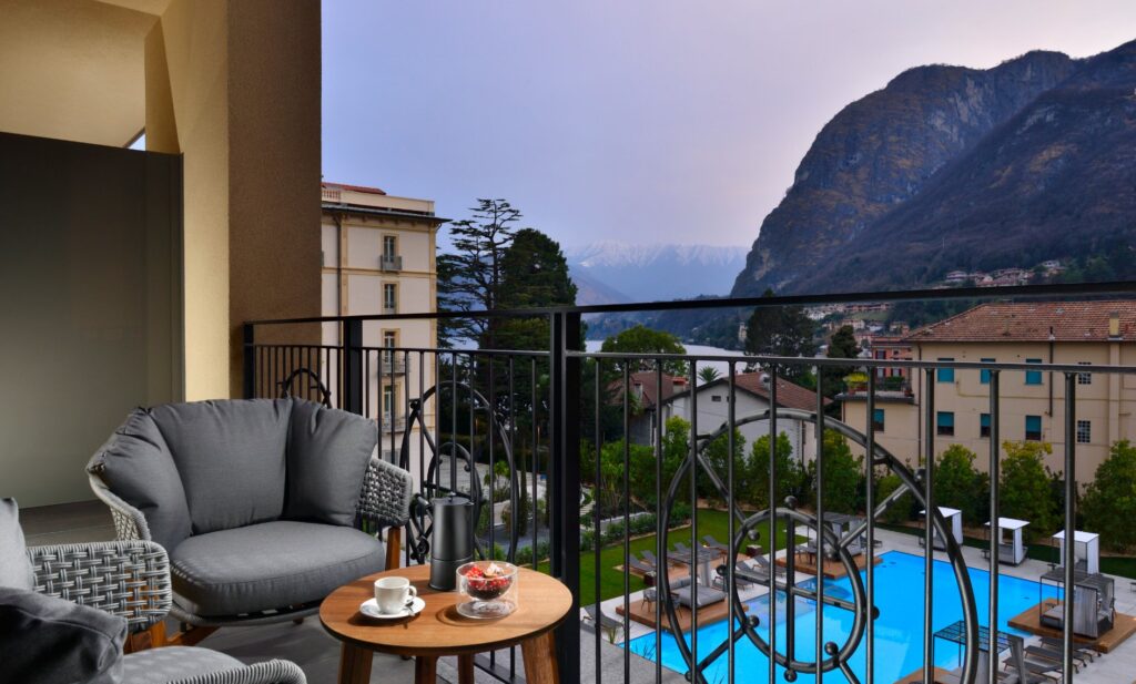 a chair and table on a balcony overlooking a pool and mountains