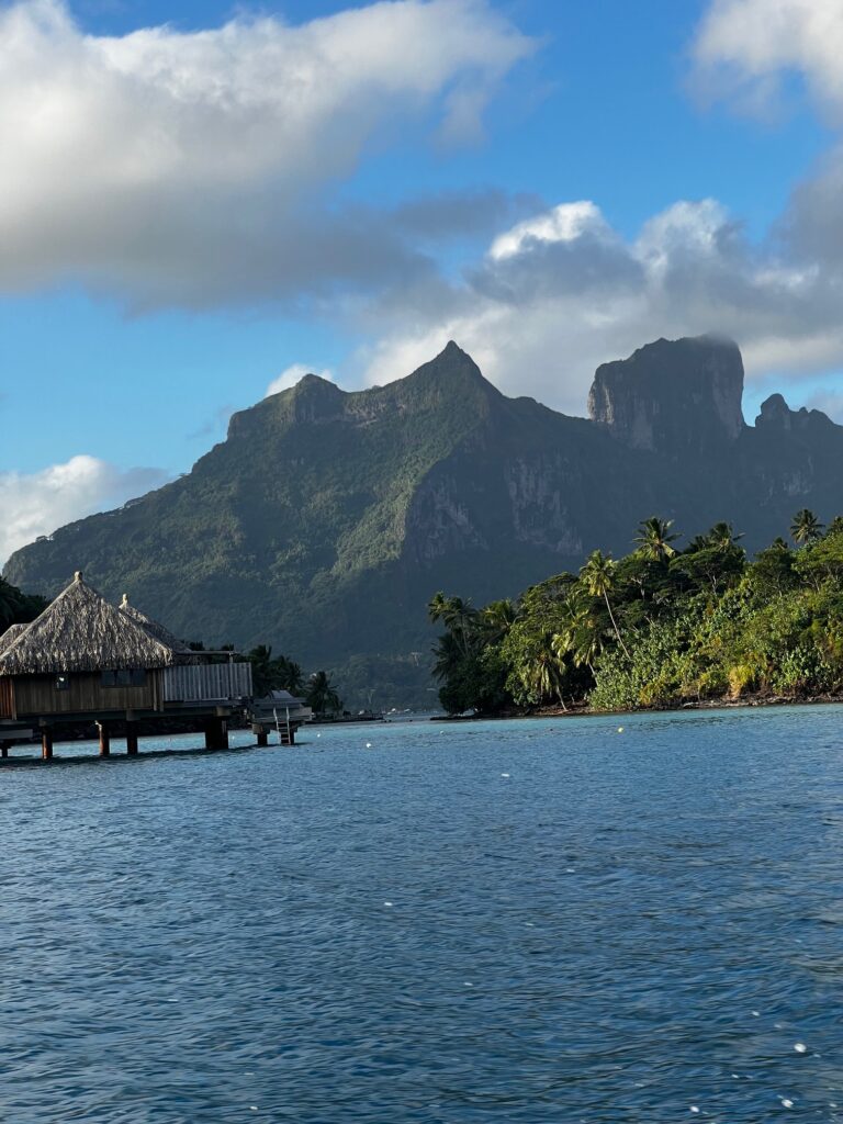 a hut on a dock in the water with mountains in the background