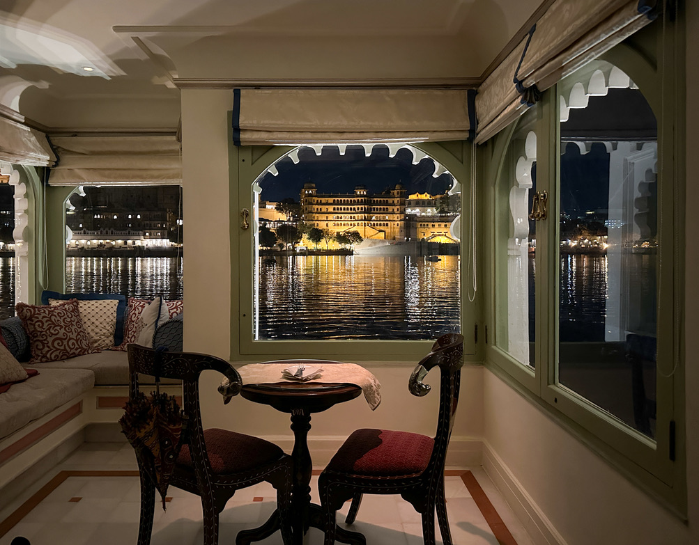 a table and chairs in a room with a view of a city and waterTaj Lake Palace Review