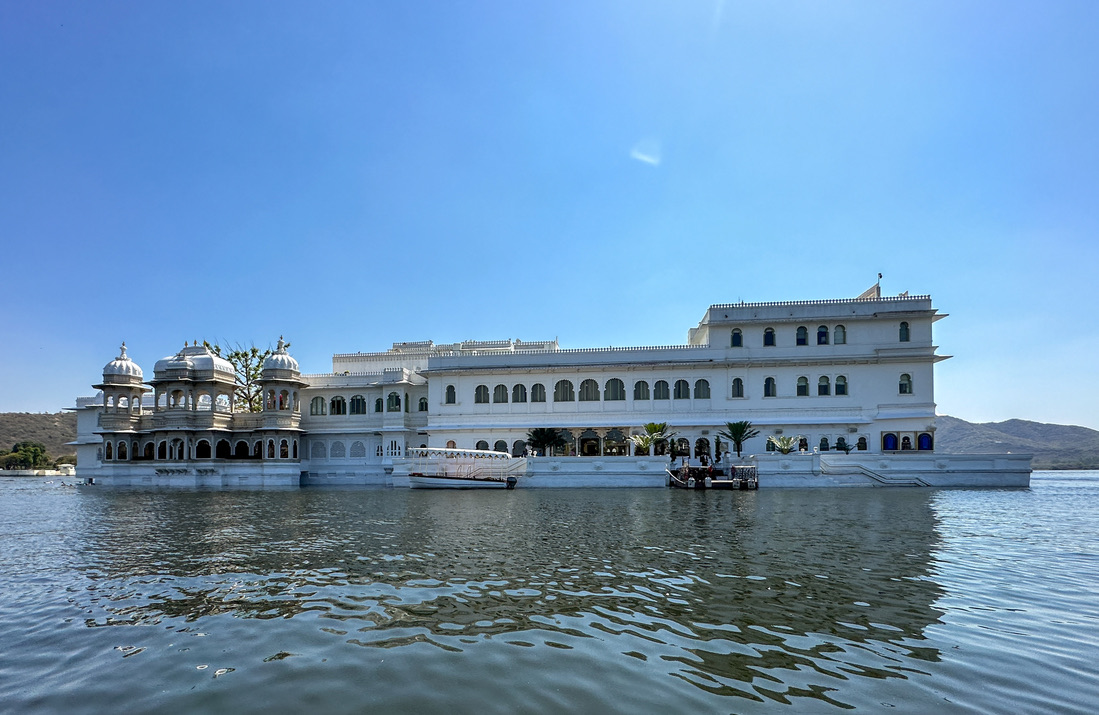 a large white building with a boat on the water with Lake Palace in the background