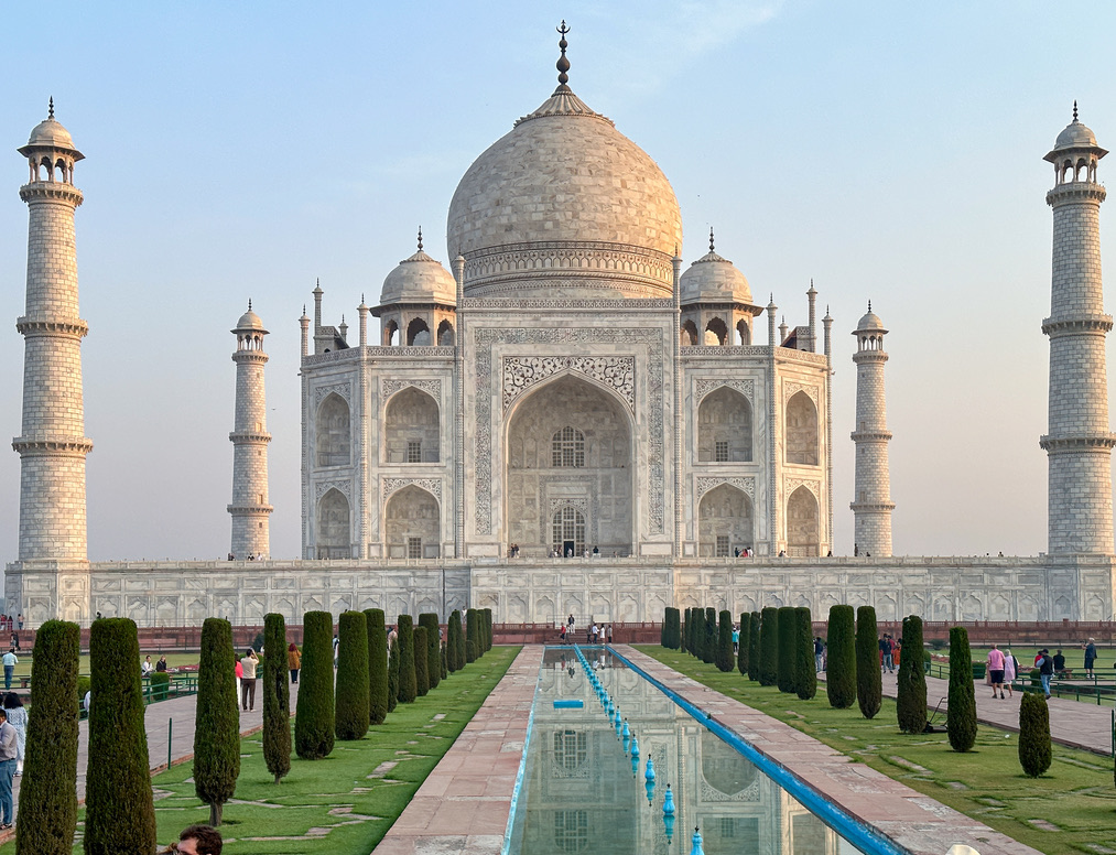 a large white building with a dome and a pool of water with Taj Mahal in the background