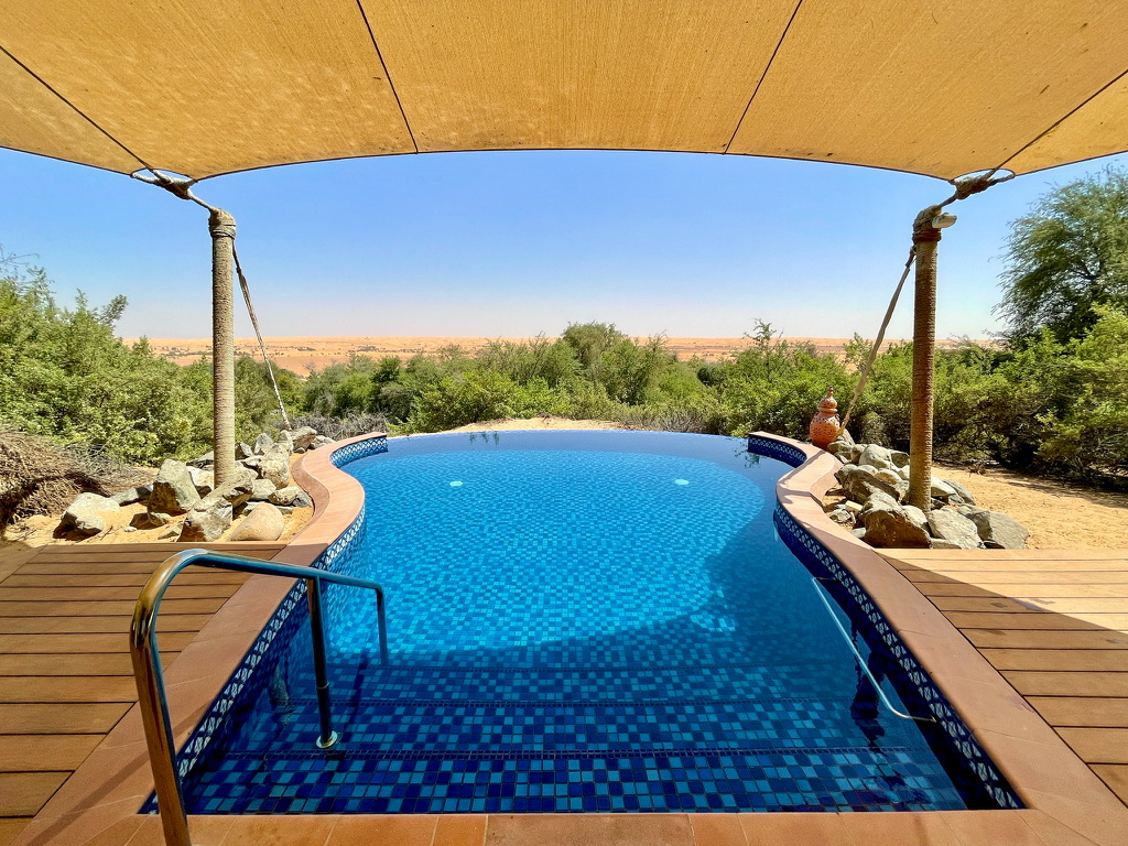 a pool with a wooden deck and a wooden deck with a wooden deck and a wooden deck with a wooden deck and a large sand dune and a desert landscape