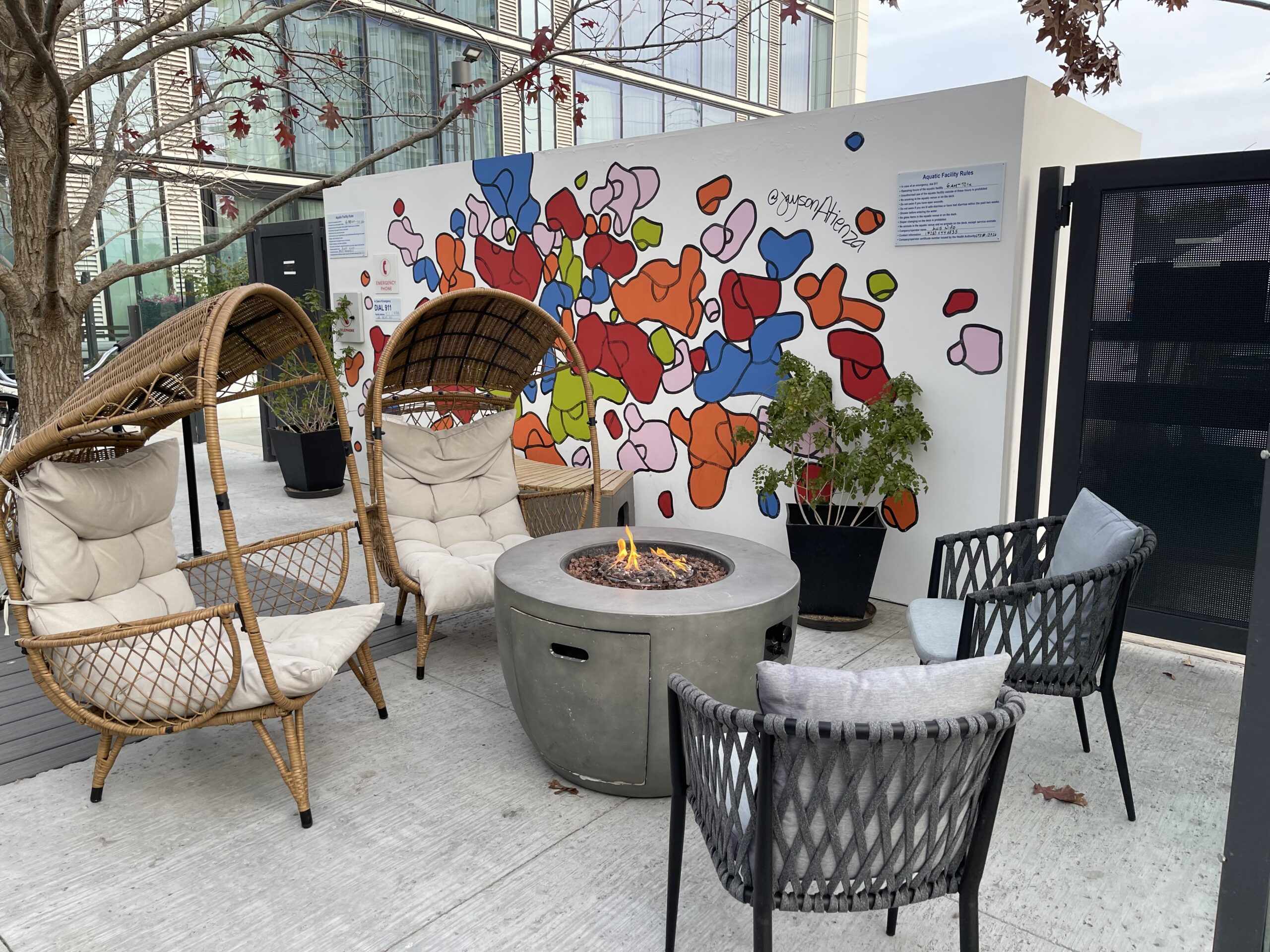 a fire pit with chairs and a wall with a painting on the wall