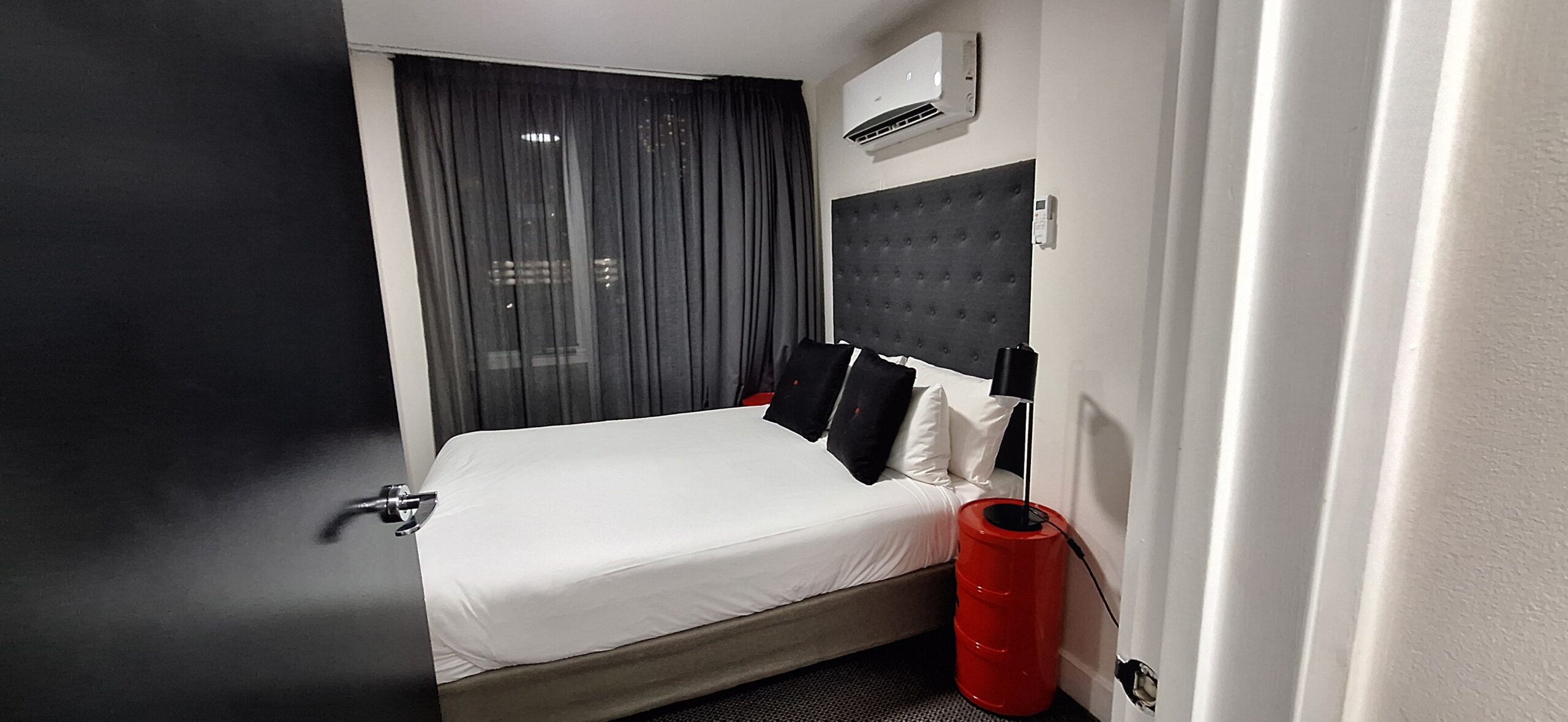 a bed with white sheets and black pillows in a room with a red barrel