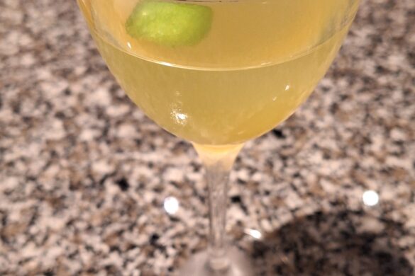 a glass of yellow liquid with a lime slice on top of it