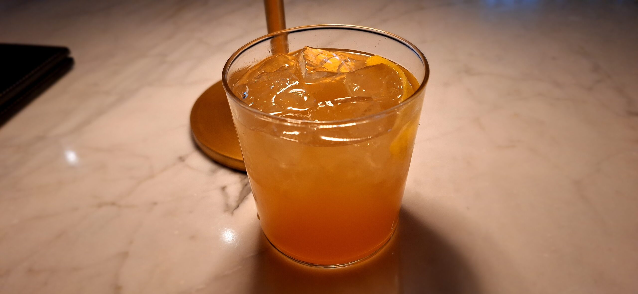 a glass of orange liquid with ice and lemon