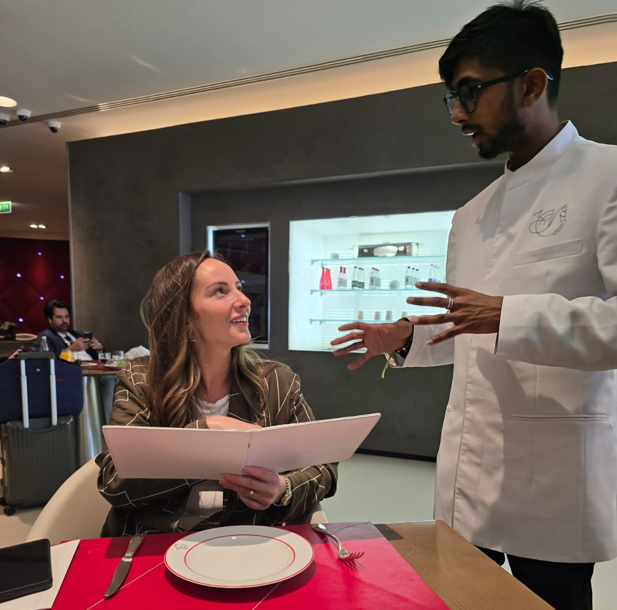 a man in a white coat talking to a woman in a restaurant