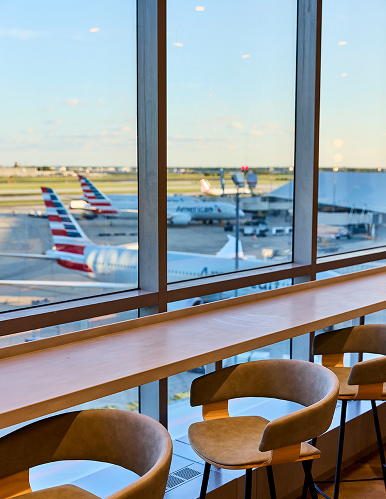 American Flagship Lounge PHL a table with chairs and a table with chairs in front of a window with airplanes in the background