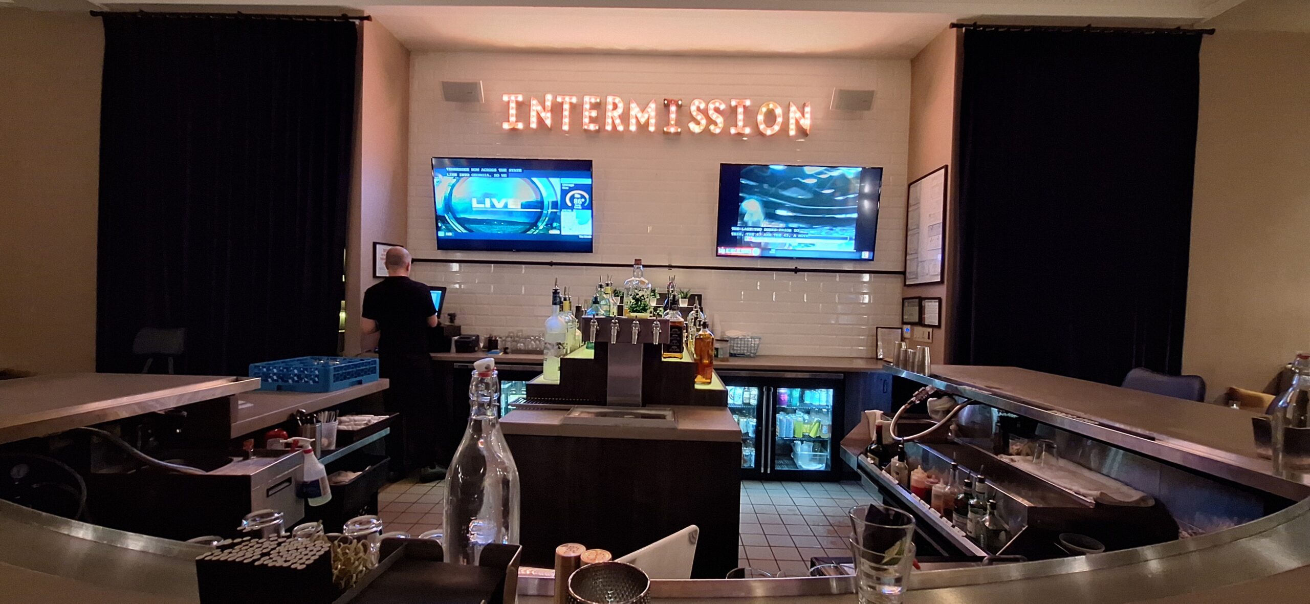 Cambria Hotel Chicago a bar with two monitors and a man standing behind it