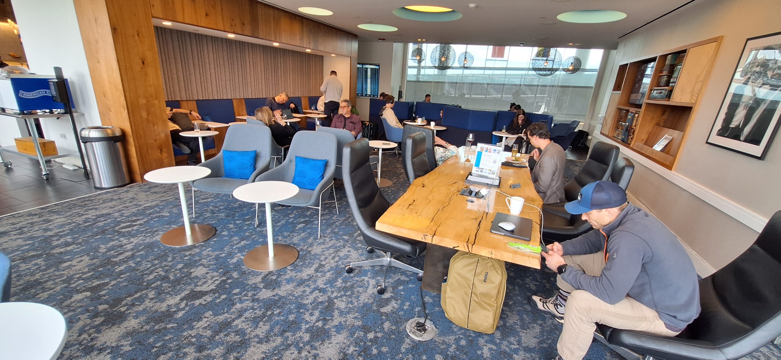 Centurion Lounge Philadelphia a group of people sitting at tables in a room with blue couches