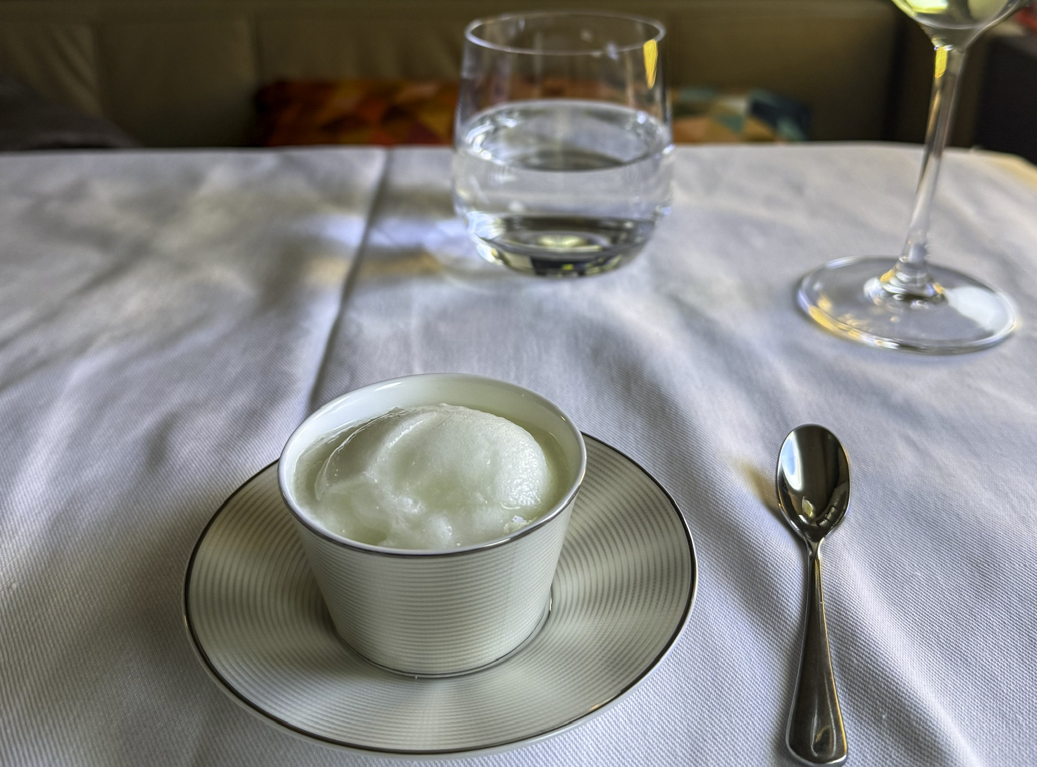 a bowl of ice cream on a plate with a spoon and a glass of water