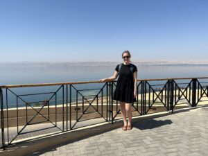 a woman standing on a walkway with a railing and a body of water in the background