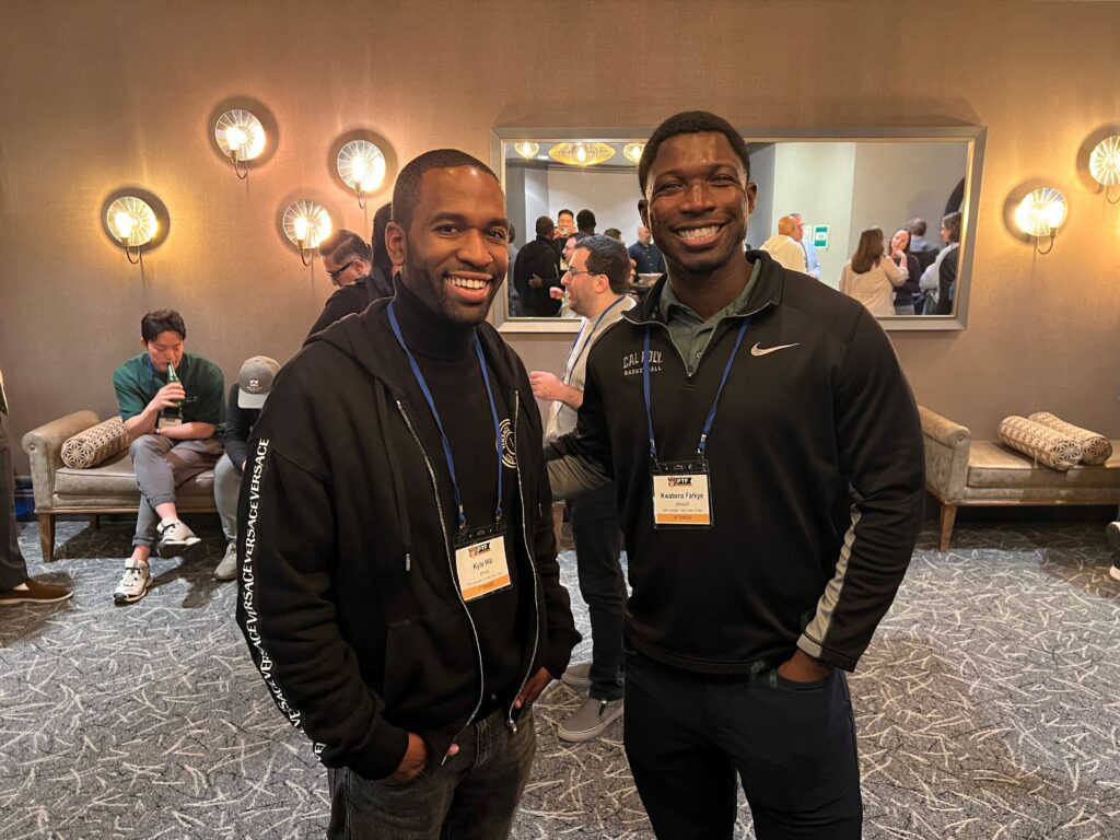two men standing in a room with people around them