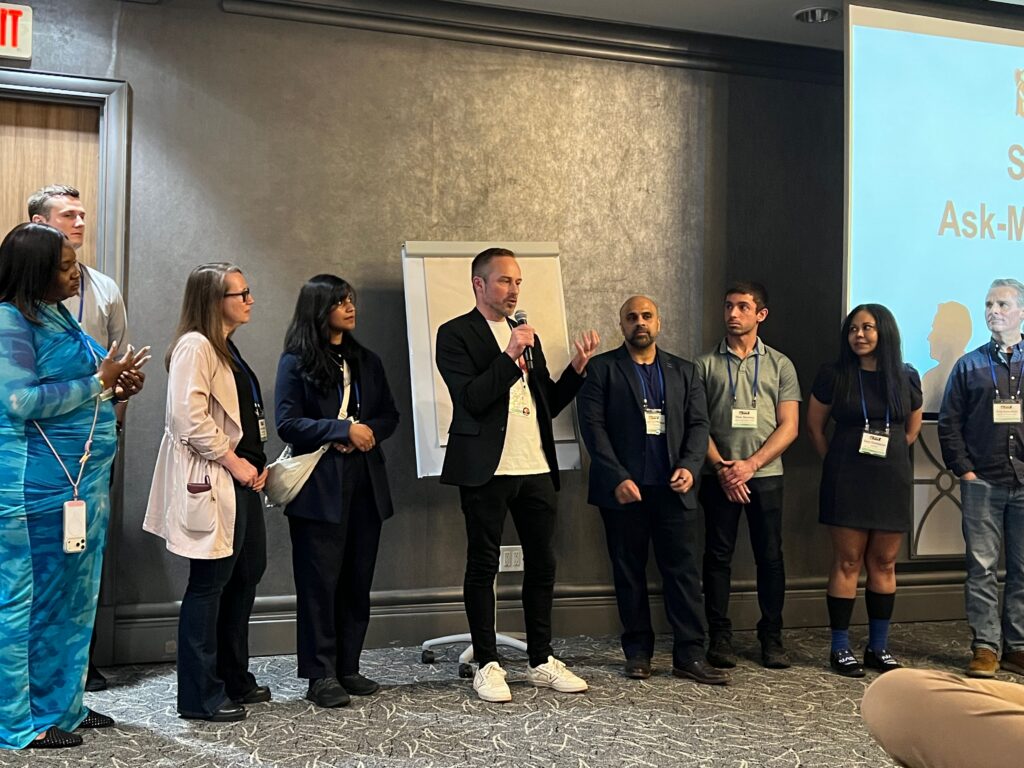 a group of people standing in front of a man speaking