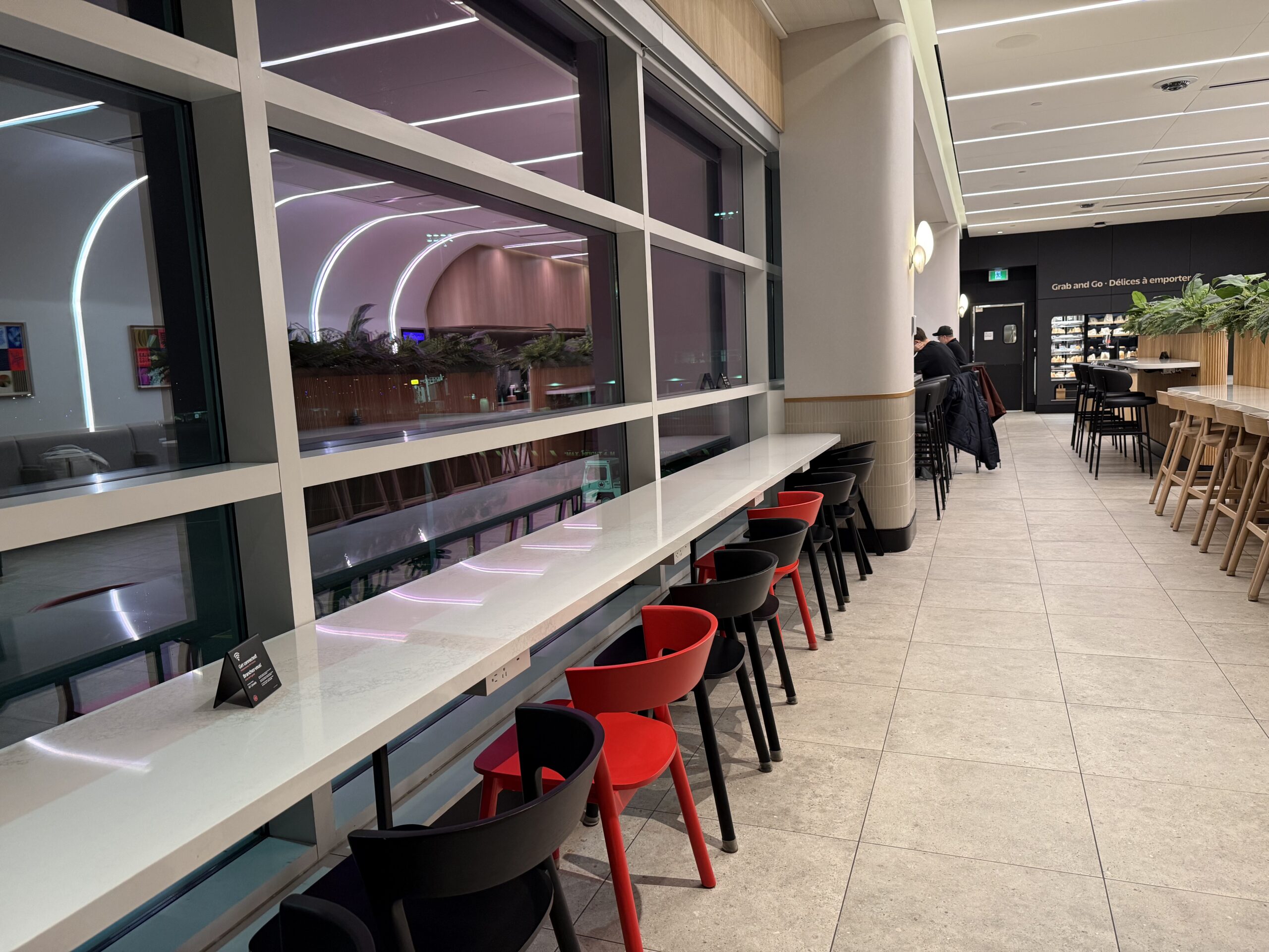Air Canada Cafe YVR C47 a long white counter with red and black chairs in a room with a large window
