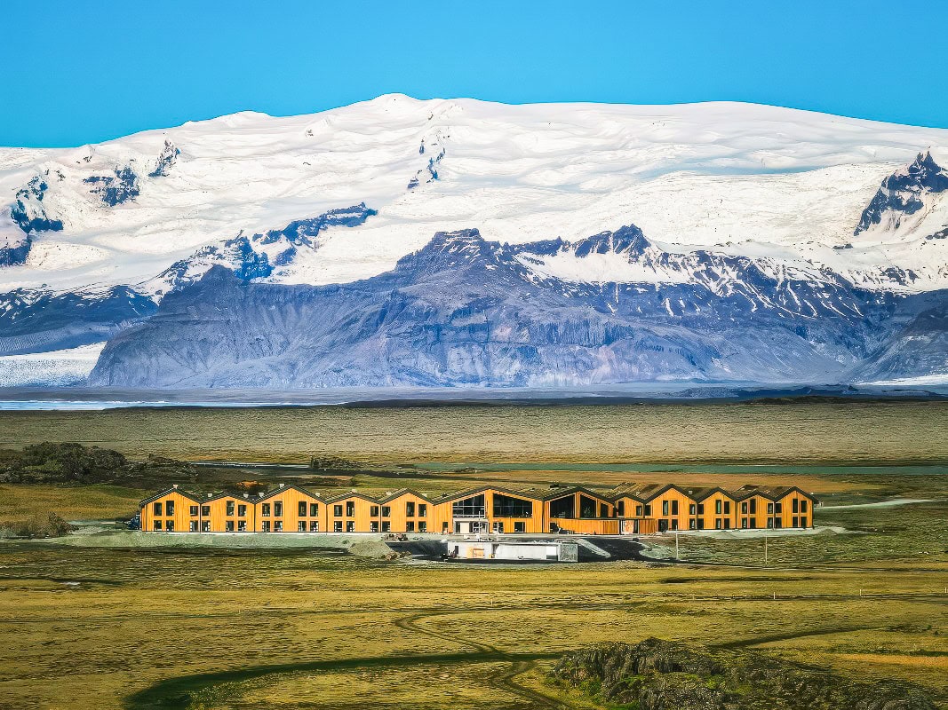 a building in the middle of a field with a snowy mountain in the background