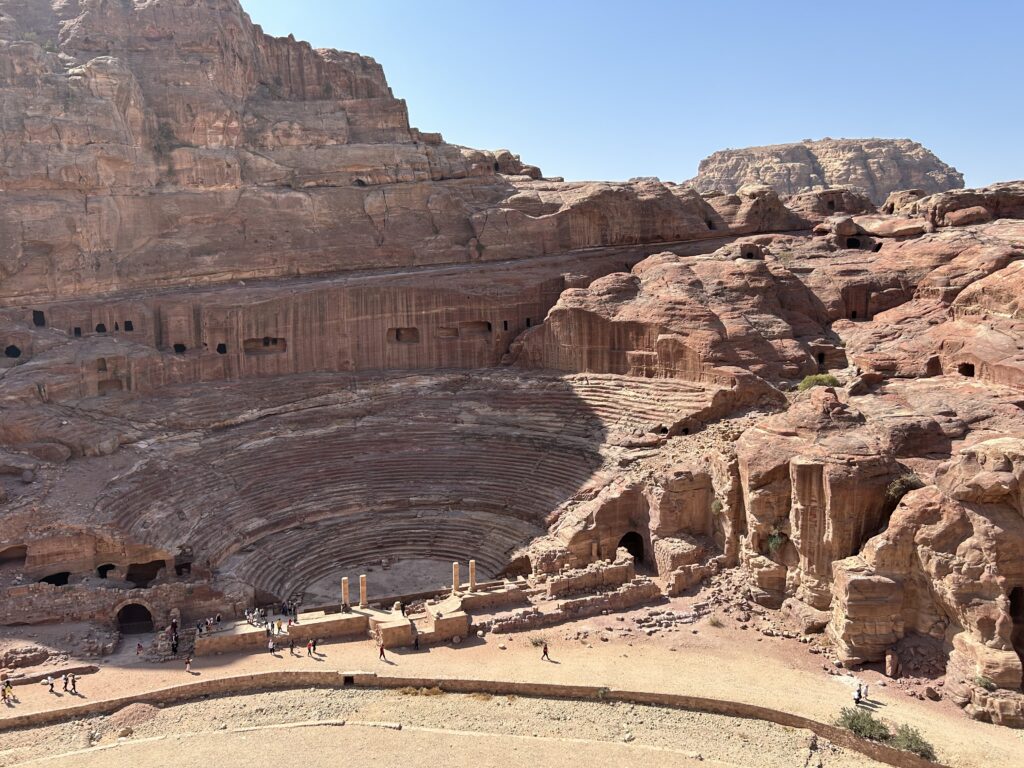 a large stone amphitheater in a rocky landscape with Petra in the background