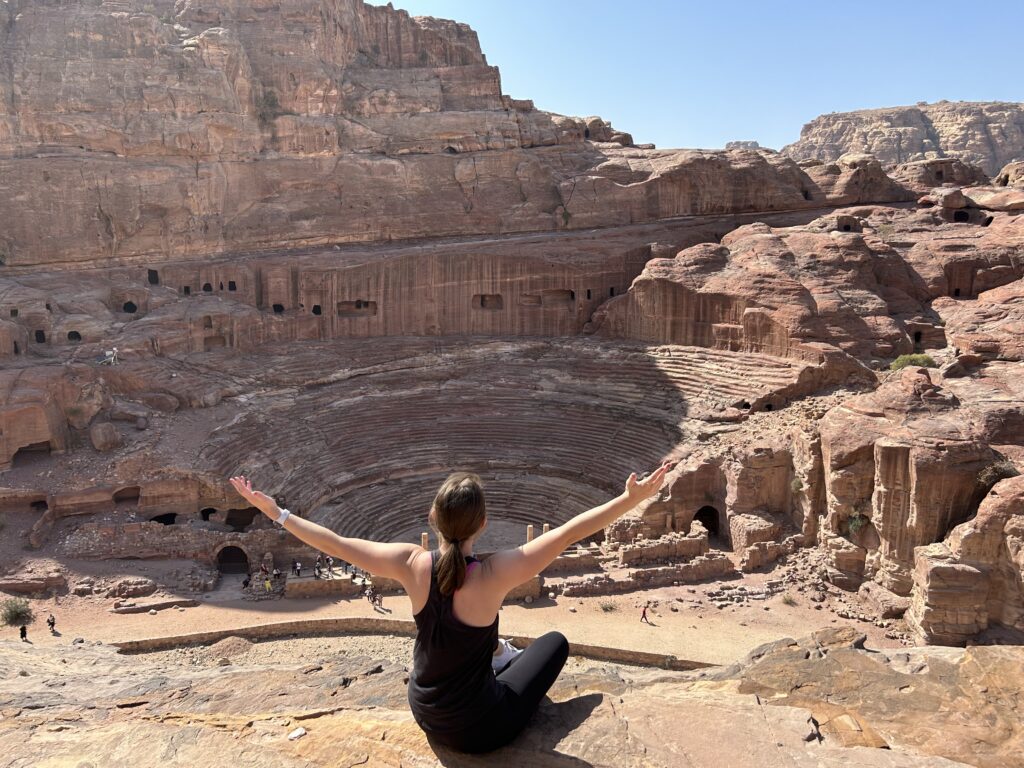 a woman sitting on a rock ledge with her arms out in the air